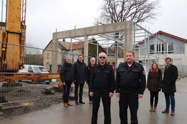 Mit dem Kran (links) entsteht die neue Fahrzeughalle. Darüber freuen sich (von links) Thorsten Paulussen, Matthias Kalkreuter, Andreas Naumann vom Gebäudemanagement, Friedhelm Stölting, Andreas Bicker sowie Janina Fleischhammer und Thorsten Hoffjann vom Architekturbüro Hoffjann. Rechts im Hintergrund ist das bestehende Gerätehaus zu sehen. - © Nadine Uphoff
