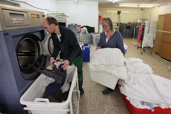 Der Betrieb am neuen Standort in der Saganer Straße läuft an. Wäschereileiter Stanislav Fuchs entleert eine Profiwaschmaschine, während Geschäftsführerin Marie-Luise Bolle schon den nächsten Korb Schmutzwäsche bereithält. - © Bernhard Preuss