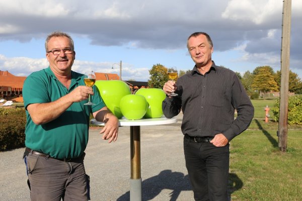 LWL-Ziegeleimuseums Geschäftsführer Willi Kuhlke (rechts) und Garten und Landschaftsbauer Frank Wilhelmi (links) stoßen mit einem Apfelsaft auf das kommende "Himmel und Erde"- Fest an: Beide werden in der Jury zur Wahl des "Besten Lippischen Apfelsaftes" sitzen, für den die glänzenden Pokale in Apfelform (Mitte) vorgesehen sind. - © Alina Hetland