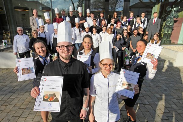 Garniert mit ihren hohen Mützen, stehen als beste Köche Matthias Büker und Lena Kendon vorn, gefolgt von den Siegern bei den Hotel- und Restaurantfachleuten Doreen Endryk, Chiara Castello und Silvija Tarutyke. Den Fonds bilden die weiteren Teilnehmer und Juroren. - © Bernhard Preuss