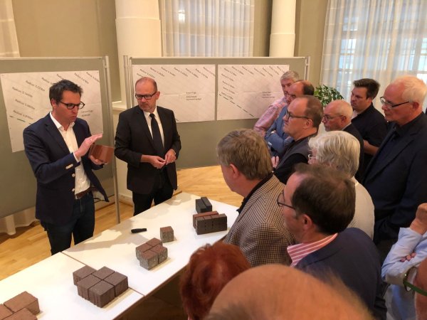 Dieser Stein soll es sein: Landschaftsarchitekt Nils Kortemeier (links) beschreibt im Kurhaus die Eigenschaften des roten Klinkers, für den sich die Politik im Anschluss entscheiden wird. Neben Kortemeier steht der Technische Beigeordnete der Stadt, Bernd Zimmermann. - © Thomas Reineke