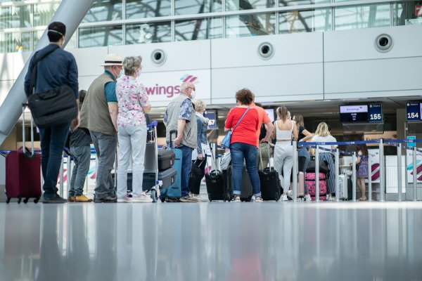 Reisende stehen mit ihrem Gepäck an den Check-In-Schaltern am Flughafen. - © picture alliance/dpa