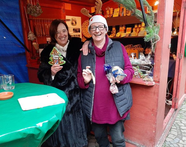 Regina Zelms (links, Kelter und Kultur Verein) und Margarida Pogarell (Autorin aus Portugal) zeigen  lokale Spezialitäten wie Bonbons, Fisch und Lebkuchen.  - © Julia Kube