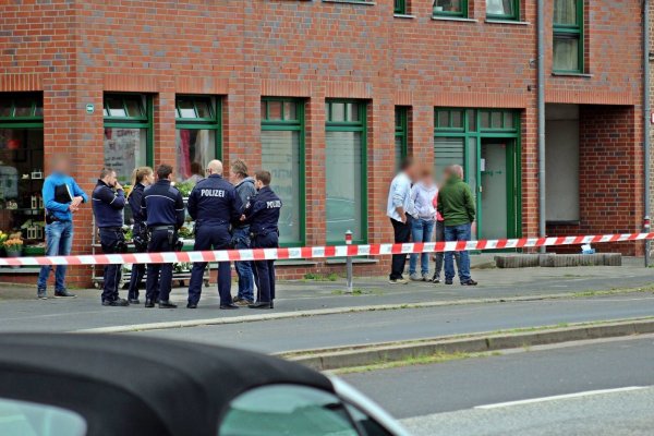 Polizisten und Passanten stehen vor einem Haus in der Innenstadt von Neuss. Nach Schüssen ist eine 27-jährige Frau gestorben. - © dpa