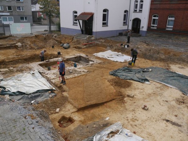 Blick von Nord-Osten auf die Grabungsfläche: In der Mitte zeichnet sich die dunkle Verfärbung des Abgrenzungsgraben, im Hintergrund die neuzeitlichen, bisher unbekannten Kellerräume, die während der Ausgrabung zutage getreten sind. - © EggensteinExca/Süße