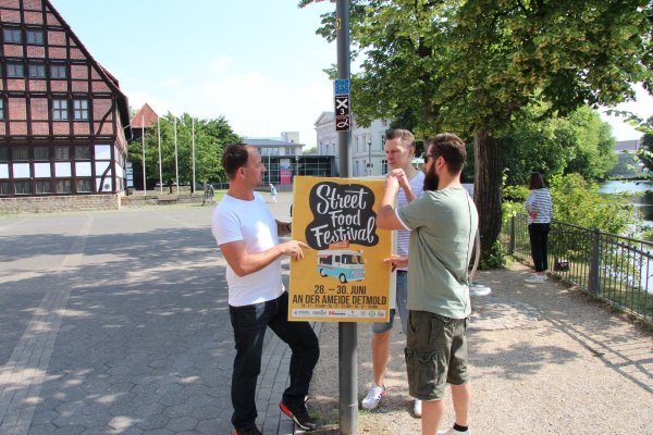 Werben für die Veranstaltung: (von links) Karsten Arning („Stadtlicht" Lemgo), Johannes Strake („Hermanns Club") und Rico Falk („Burrico") hängen an der Ameide ein Plakat auf. Kommendes Wochenende findet hier das Street-Food-Festival statt. - © Jana Beckmann