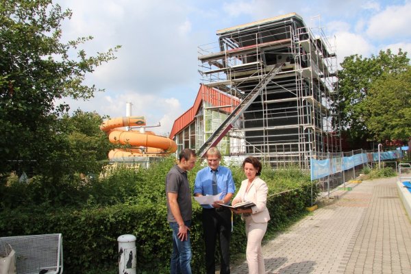 An der Baustelle: (von links) stellvertretender Badleiter Christian Herrmann, Stadtwerke-Geschäftsführer Jörg Karlikowski und Stadtwerke-Pressesprecherin Eva Ellminger besprechen den Fortschritt der Arbeiten. Im Hintergrund sind (rechts) der neue Rutschenturm und (links) die alte Rutsche, die überarbeitet wird, zu sehen. - © Jana Beckmann