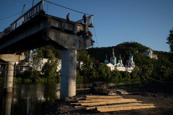 Bauarbeiter steigen von einer Leiter auf einer zerstörten Brücke neben dem Kloster Swjatohirsk herunter. - © Bram Janssen/AP/dpa