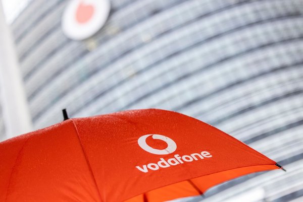 Ein Passant geht mit einem aufgespanntem Regenschirm mit dem Logo von Vodafone an der Zentrale der Deutschlandtochter des britischen Vodafone-Konzerns vorbei. - © Thomas Banneyer/dpa