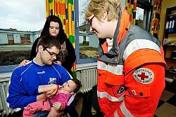 Hochwassergeschädigt, aber gut drauf: Lena-Fabienne Bauer, Mutter Marina Scheliong und Vater Florian Bauer. Nina Kleiszmantat (rechts) hat bei der Übung für die Kleine Babynahrung und Windeln besorgt. - © 