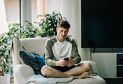 Ein junger Mann sitzt mit Smartphone auf einem Sessel - Zacharie Scheurer/dpa-tmn