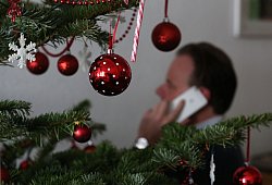 Mann telefoniert neben einem Weihnachtsbaum - Ina Fassbender/dpa-tmn