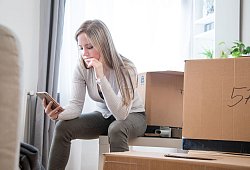 Eine Frau sieht zwischen Umzugskartons auf ein Handy - Christin Klose/dpa-tmn