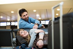 Ein Mann weckt eine Frau im Wartebereich eines Flughafen - Christin Klose/dpa-tmn