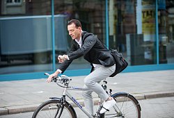 Mann fährt mit Fahrrad durch Stadt und guckt auf Uhr - Christin Klose/dpa-tmn