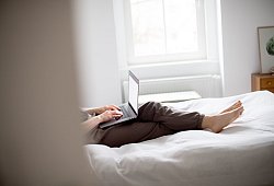 Eine Frau sitzt mit Laptop auf einem Bett - Zacharie Scheurer/dpa-tmn