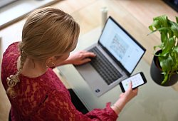 Frau sitzt vor einem Laptop und schaut auf ein Smartphone - Helena Dolderer/dpa/dpa-tmn