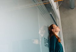 Eine Frau lehnt ersch&ouml;pft an einer Glaswand im B&uuml;ro - Zacharie Scheurer/dpa-tmn