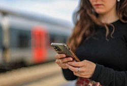 Eine junge Frau steht mit ihrem Mobiltelefon auf einem Bahnsteig - Jan Woitas/dpa/dpa-tmn