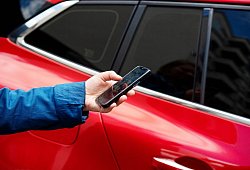 Eine Person steht mit einem Smartphone neben einem Auto - Bernd Diekjobst/dpa-tmn