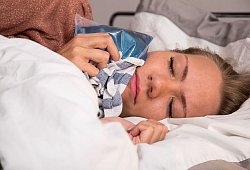 Eine Frau hält sich im Bett einen Kühlakku an die Wange - Christin Klose/dpa Themendienst/dpa-tmn