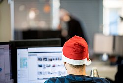 Ein Mann sitzt mit Weihnachtsm&uuml;tze im B&uuml;ro - Zacharie Scheurer/dpa-tmn