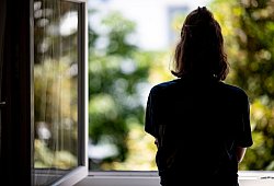 Eine junge Frau steht in ihrer Wohnung an einem Fenster - Fabian Sommer/dpa/dpa-tmn