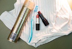 Lippenstift, Haarspray und eine Zahnb&uuml;rste liegen auf einem Shirt - Christin Klose/dpa-tmn