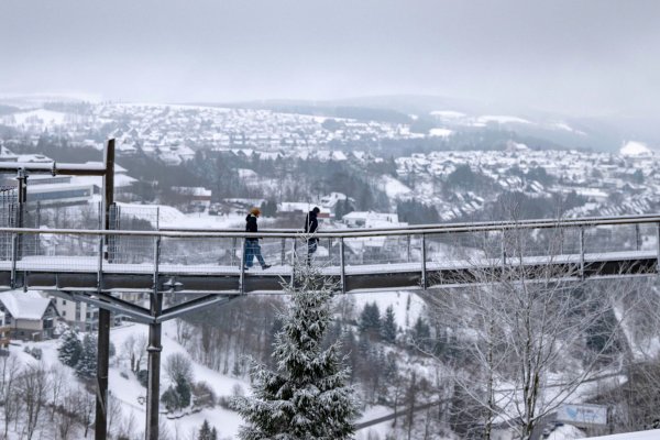 Spaziergänger gehen eine Brücke neben der Winterberger Bobbahn mit Blick auf die Landschaft im Schnee. - © David Inderlied/dpa