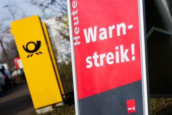 Ein Warnstreik-Schild bei einem Post-Standort, daneben ein Briefkasten - im Ringen um einen Tarifabschluss haben Tausende Postler erneut die Arbeit niedergelegt. - © Philipp von Ditfurth/dpa