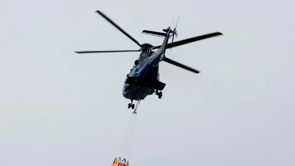 Ein Löschhubschrauber der Bundespolizei fliegt über dem Zeithainer Tagebau und nimmt Wasser auf, um den Waldbrand Gohrischheide zu bekämpfen. - © Daniel Wagner/dpa