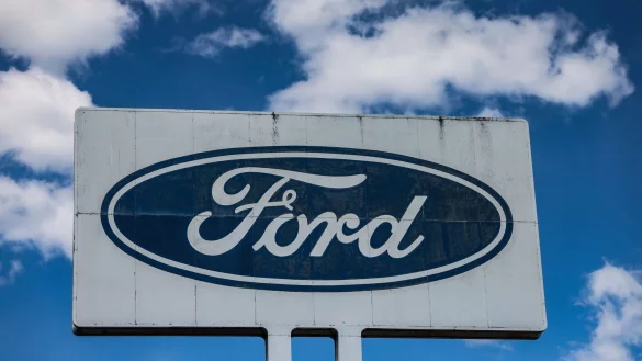 Ein Logo steht vor dem Ford Werk bei gutem Wetter - wirtschaftlich gesehen sind die Perspektiven des Ford-Autogeschäfts in Europa düster. - © Oliver Berg/dpa