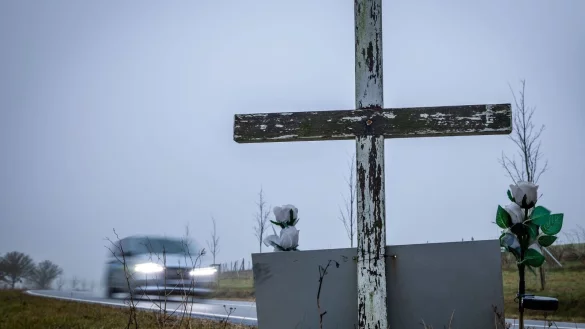 in Auto fährt auf einer Landstraße an einem hölzernen Kreuz vorbei, welches zur Erinnerung an ein Unfallopfer aufgestellt wurde. - © Jens Büttner/dpa