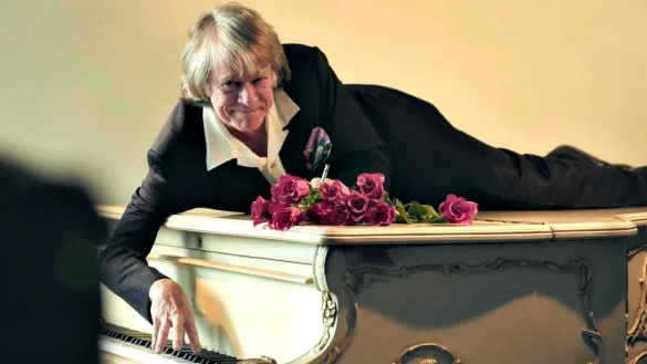 Helge Schneider liegt auf einem Klavier in einer Szene des Films «Helge Schneider - The Klimperclown», der nun in der Mediathek zu sehen ist und am Mittwoch, 20.8., im Ersten gezeigt wird. - © -/SWR Presse/Bildkommunikation/dpa