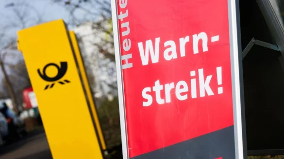 Ein Warnstreik-Schild bei einem Post-Standort, daneben ein Briefkasten - im Ringen um einen Tarifabschluss haben Tausende Postler erneut die Arbeit niedergelegt. - © Philipp von Ditfurth/dpa