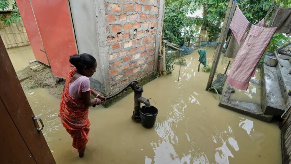 Eine Frau versucht in der überfluteten Umgebung ihres Hauses, Wasser zu sammeln. - © Uncredited/AP/dpa