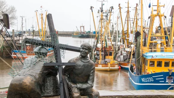 Schwarze Holzkreuze lehnen an der Bronezeskulptur &laquo;Alt- und Jungfischer&raquo; im Hafen in Neuharlingersiel. Das Fischen mit Grundschleppnetzen steht in der Kritik. - &copy; Lennart Stock/dpa