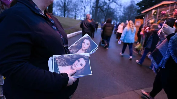 Eine Frau h&auml;lt Flyer mit einem Bild von Lisa Marie Presley, w&auml;hrend Menschen an ihr vorbeigehen, um in Graceland an einem Gedenkgottesdienst teilzunehmen. - &copy; John Amis/FR69715 AP/dpa