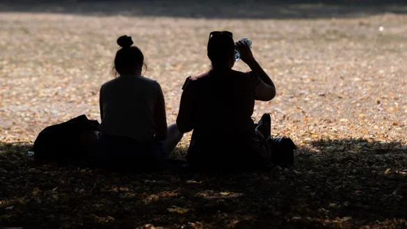 Zwei Frauen sitzen in einem Park im Schatten der B&auml;ume, um sich vor der Hitze zu sch&uuml;tzen. - &copy; Friso Gentsch/dpa