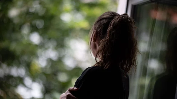 Eine Jugendliche steht gedankenversunken am Fenster. Selbstverletzendes Verhalten kann vorübergehend negative Gefühle verdrängen. - © Fabian Sommer/dpa/dpa-tmn