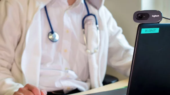 Ein Hausarzt sitzt während einer Videosprechstunde in seiner Praxis vor einem Laptop. - © Monika Skolimowska/ZB/dpa