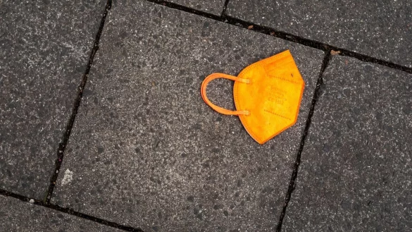 Ein gebrauchter orangefarbener Mund-Nasen-Schutz liegt auf dem Gehweg. - &copy; Peter Kneffel/dpa/Symbolbild