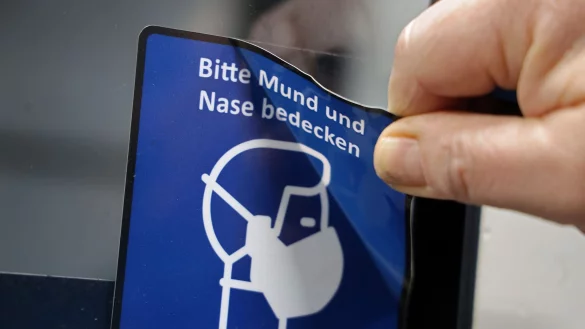 Es wird an einer Stra&szlig;enbahn-T&uuml;r ein Piktogramm mit dem Hinweis auf die Maskenpflicht entfernt. - &copy; Bernd W&uuml;stneck/dpa/Archivbild