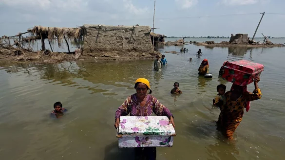 Frauen tragen Habseligkeiten aus ihrem durch heftige Regenfälle überschwemmten Haus im Bezirk Qambar Shahdadkot in der pakistanischen Provinz Sindh. - © Fareed Khan/AP/dpa