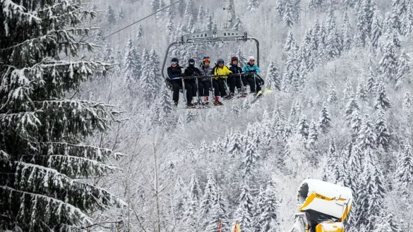 Skifahrer fahren bei winterlichem Wetter in einem Sessellift an einer Schneekanone vorbei. - &copy; Bernd Thissen/dpa/Archivbild
