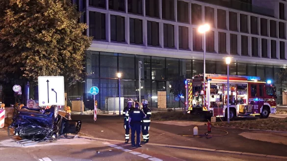 Einsatzkräfte der Feuerwehr und Polizei stehen neben einem zerstörtem Wagen an der Unfallstelle in München. - © -/Berufsfeuerwehr München/dpa