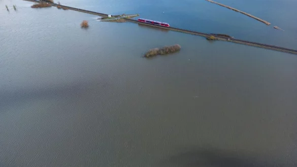 Ein Personenzug der Deutschen Bahn f&auml;hrt im Januar 2023 durch eine &uuml;berschwemmte Flussniederung bei Eichen in Hessen. - &copy; Boris Roessler/dpa