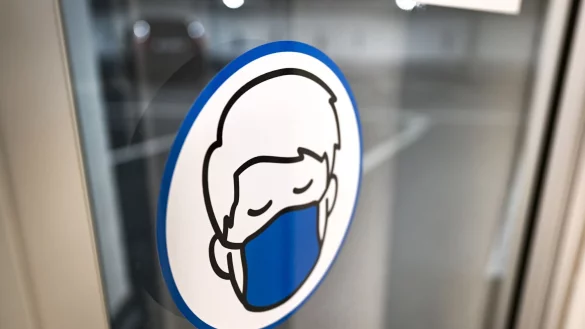 Ein Aufkleber an einer Glast&uuml;r weist auf das Tragen einer Maske hin. - &copy; Felix K&auml;stle/dpa/Symbolbild