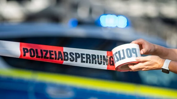 Ein Absperrband wird vor einem Polizeiwagen ausgerollt. - &copy; David Inderlied/dpa/Illustration