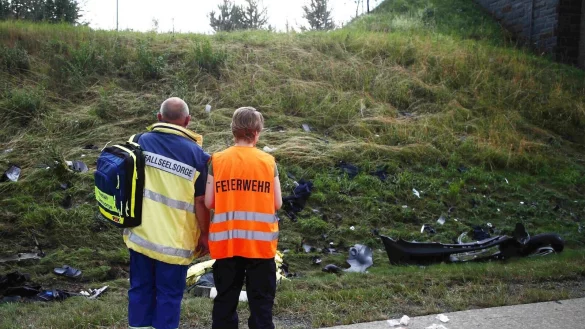 Ein Seelsorger und ein Mitglied der Feuerwehr an einer Unfallstelle auf der Autobahn 9 vor einer B&ouml;schung, die mit Tr&uuml;mmerteilen &uuml;bers&auml;t ist. - &copy; Bodo Schackow/dpa